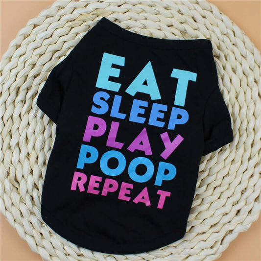 Black pet shirt with colorful text 'EAT SLEEP PLAY POOP REPEAT' on a woven mat.