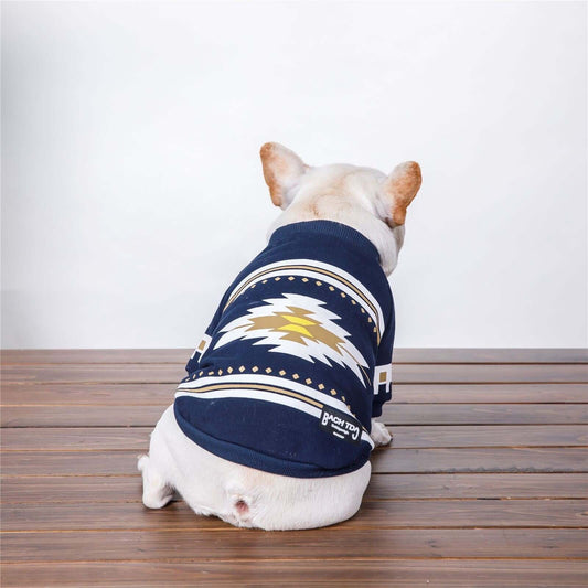 Dog wearing a navy blue sweater with white and gold patterns on a wooden floor.