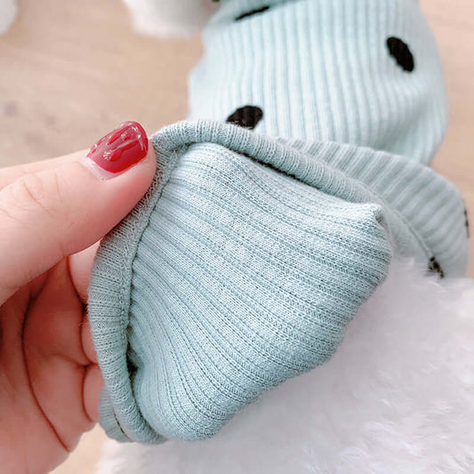 Light blue baby sock with black spots held by a hand against a white background