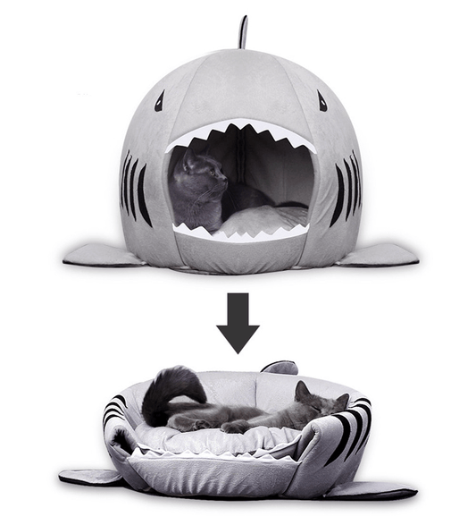 Two-in-one pet bed in shark shape shown in upright cave mode and flattened into an open cushion, featuring a relaxed gray cat lounging inside.