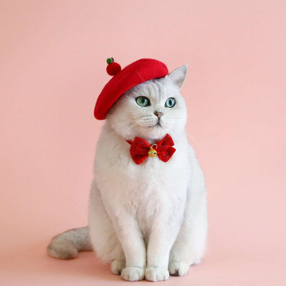 A red apple-shaped cashmere beret for cats, placed on a soft pink background, styled for winter or festive wear.