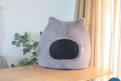Cat sleeping inside cozy semi-enclosed plush bed with ear design